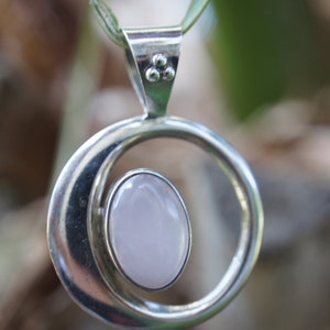 May include: A silver pendant necklace with a pale pink oval gemstone set in a circular frame.