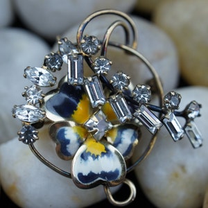 May include: A gold-tone brooch featuring a blue and yellow enamel flower with a cluster of clear rhinestones.