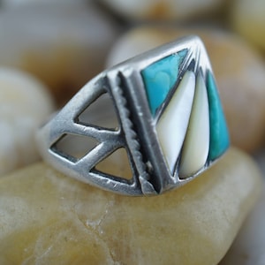May include: A silver ring with a geometric design featuring turquoise and mother-of-pearl inlay.