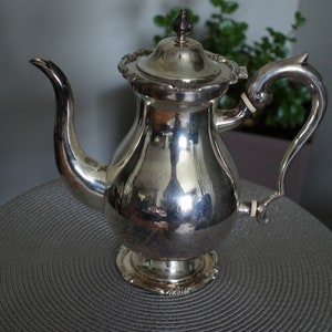 May include: A silver teapot with a round body and a curved spout. The teapot has a decorative handle and a lid with a finial.