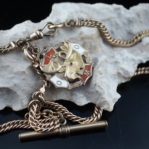 May include: A gold pocket watch chain with a decorative fob featuring a moose head and the letters L.A.P.O.M. The chain has a twisted rope design and a sliding T-bar clasp.