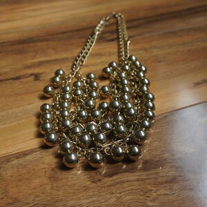 May include: A gold necklace with multiple strands of small, round beads. The necklace is layered and has a cascading effect.