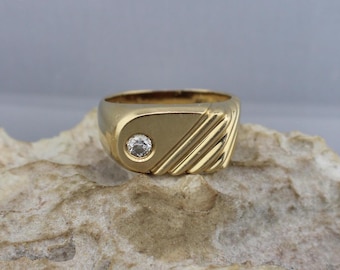 May include: A gold ring with a single round diamond set in the center. The ring has a textured, grooved design on the top.
