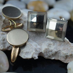 Peut inclure: Un ensemble de quatre boutons de manchette dorés. Deux boutons de manchette sont ronds et deux sont carrés. Les boutons de manchette sont sur une surface rocheuse blanche.