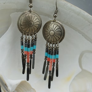 Puede incluir: Pendientes de plata con cuentas de turquesa y coral. Los pendientes tienen un dije redondo de plata con un diseño floral.