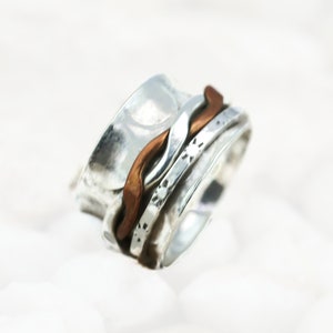 May include: A silver and copper spinner ring with a wavy design. The ring is made of multiple bands that spin around each other.