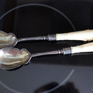 May include: A set of two silver salad servers with ivory handles. The servers have a traditional design and are in good condition.