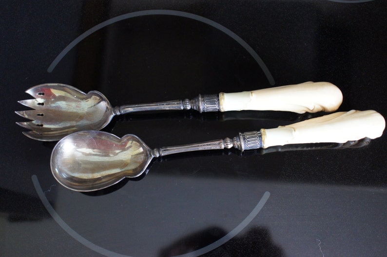 May include: A set of two silver salad servers with ivory handles. The servers have a traditional design and are in good condition.