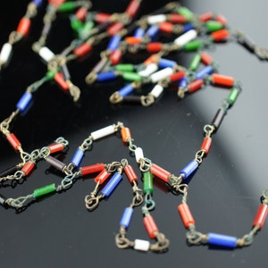 Puede incluir: Un collar de cuentas de vidrio multicolores con cuentas rojas, azules, verdes, blancas y negras. Las cuentas están conectadas por una cadena plateada.