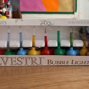 May include: A rectangular white box containing 10 Silvestri bubble lights for indoor use. The box features a clear plastic window displaying colorful glass bubble light bulbs in red, green, blue, and yellow, along with a coiled dark green wire.