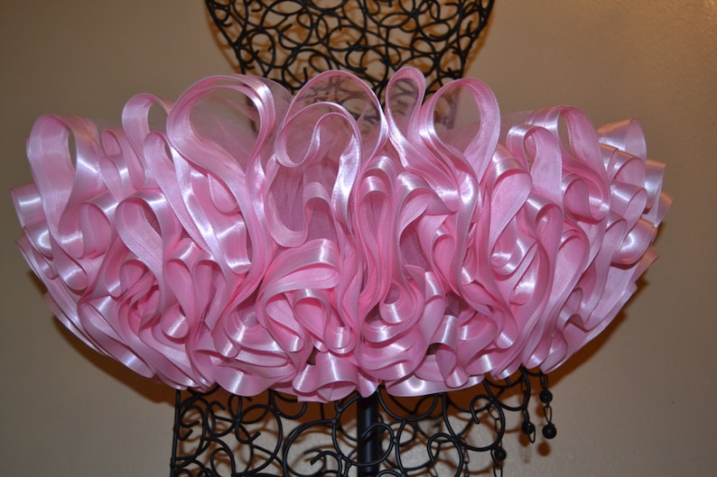 May include: A pink tulle skirt with multiple layers of satin ribbon. The skirt is displayed on a black mannequin.