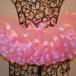 May include: A pink tulle tutu skirt with a satin ribbon trim. The skirt is layered and full, with a soft and delicate look.