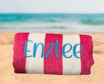 May include: A pink and white striped beach towel with the name "Enzlee" embroidered in blue.