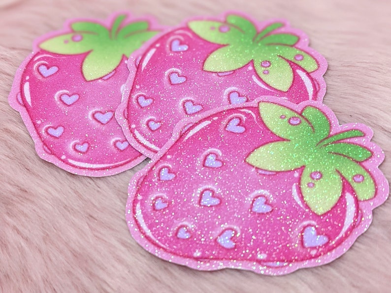 May include: Three pink glitter strawberry stickers with a green leaf and white hearts.