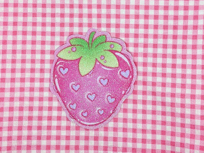 May include: A pink and green glitter strawberry with a white background. The strawberry has a green stem and leaves and is covered in small pink hearts.