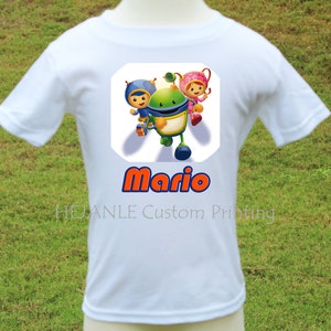 May include: White t-shirt featuring a colorful graphic of cartoon characters and the name "Mario" in orange and blue. The shirt has short sleeves and is made of a soft material. "HEANLE Custom Printing" is printed at the bottom.