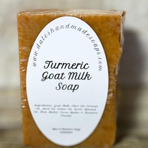 May include: A bar of turmeric goat milk soap wrapped in plastic. The soap is a light orange color and has a white label with the text "Turmeric Goat Milk Soap" and "www.daleshandmadesoaps.com".