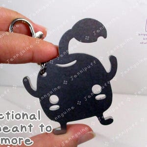 May include: A black metal keychain featuring a stylized cartoon character with a rounded body, arms, and legs. The keychain has a lobster clasp and a split ring. Text on the image reads "Functional but meant to be more aesthetic."