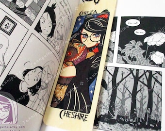 May include: A wooden bookmark featuring a colorful illustration of a woman with black hair and glasses, holding a red gem. The bookmark has the text "CEREZA CHESHIRE" printed on it.