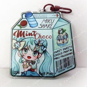 May include: A blue and green milk carton-shaped acrylic charm featuring a cartoon character holding a green ice cream cone. The charm has the text "Miku Shake" and "Mint Choco" on it. The charm also has a barcode and the text "Sweet Sweets Choco Mint Miku Milkshake".