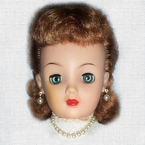 May include: A vintage doll with brown hair, blue eyes, and a pearl necklace. The doll is wearing a white dress.