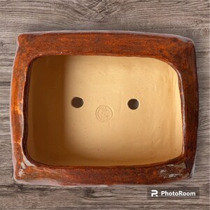 Può includere: Un vaso rettangolare in terracotta con una smaltatura marrone e un interno marrone chiaro. Il vaso ha due fori di drenaggio e un timbro circolare che recita "Bob's Clay".