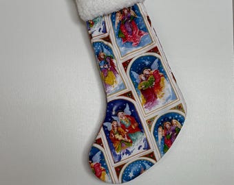 Puede incluir: Una media de Navidad blanca con un puño blanco esponjoso. La media está decorada con un patrón repetido de ángeles en marcos que parecen vidrieras.