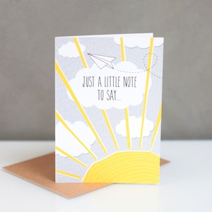 May include: A grey and yellow card with a sun, clouds, and a paper aeroplane. The text on the card reads "Just a little note to say..."