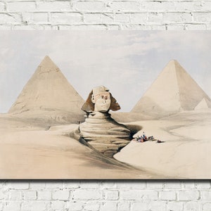 May include: An artistic print depicting the Sphinx and pyramids in Egypt. The artwork features the Sphinx in the foreground, with two pyramids in the background under a pale sky. The color palette is dominated by beige, tan, and light blue.