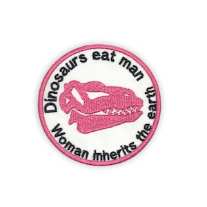 May include: Pink and white embroidered patch with the text "Dinosaurs eat man, woman inherits the earth" and a pink dinosaur skull illustration.