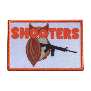 May include: Orange and white embroidered patch with an owl holding a rifle and the text "SHOOTERS" in orange.