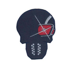 May include: A dark blue embroidered patch with a skull design. The skull has a red and white eye with a white cross over it. The skull has a white outline and a row of white dots on the bottom.