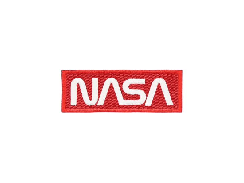 Pu&ograve; includere: Una toppa rettangolare con il logo NASA. La toppa ha uno sfondo rosso con il testo NASA bianco in grassetto, in un carattere sans-serif. &Egrave; destinata all'applicazione su abbigliamento o accessori.