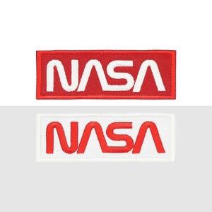 May include: Two NASA patches. One patch has a red background with white embroidered text. The other patch has a white background with red embroidered text. Both patches are rectangular.