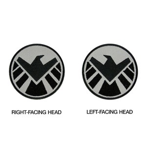 May include: Two black and white embroidered patches with the S.H.I.E.L.D. logo. The left patch has the eagle facing left, and the right patch has the eagle facing right. The text "RIGHT-FACING HEAD" is below the right patch, and the text "LEFT-FACING HEAD" is below the left patch.