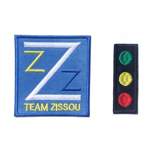 May include: Two embroidered patches, one blue with a white 'Z' and the text 'TEAM ZISSOU', the other black with a red, yellow, and green traffic light.