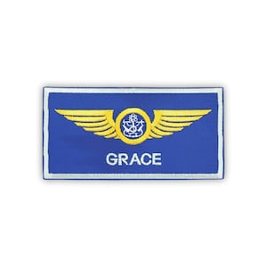 May include: A blue embroidered patch with a gold winged emblem and the name "GRACE" in white lettering. The patch has a white border.