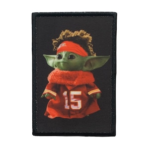 May include: A green and brown character wearing a red and yellow jersey with the number 15 on the front. The character is wearing a red headband and has brown hair. The character is on a black background.