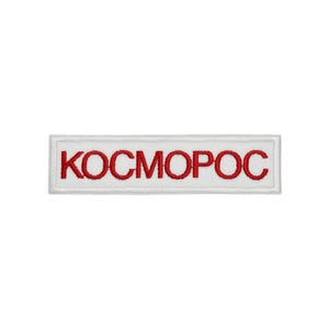 May include: A rectangular embroidered patch featuring a white background with a thin white border. The text KOCMOPOC is stitched in bold red capital letters across the centre of the patch, creating a clear contrast against the white fabric base.