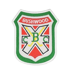 May include: Embroidered patch with a shield design. The patch features the word "BUSHWOOD" in red, a white background, and green and red accents. The center has crossed hockey sticks and the letters "CBC".