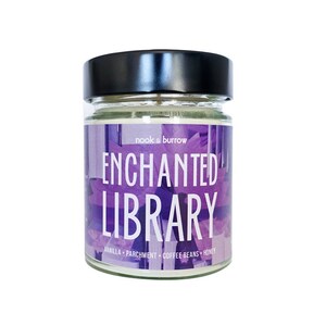 May include: A glass candle jar with a black lid. The label reads "nook & burrow ENCHANTED LIBRARY VANILLA + PARCHMENT + COFFEE BEANS + HONEY".