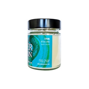 Puede incluir: Una vela de vidrio en un frasco con tapa negra. La etiqueta es de color verde azulado y verde con un patr&oacute;n de piel de serpiente. El texto de la etiqueta dice "270 ML Soy Wax Candle Made in Australia nook & burrow treat yo shelf NOOKANDBURROW.COM"