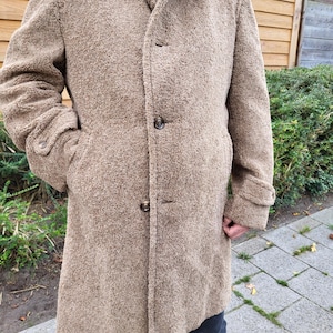 May include: A long, brown, fuzzy coat with a button closure. The coat has a collar and two pockets.