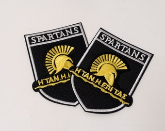 Spartaanse helm in geborduurde stoffen patch met de inscriptie Η ΤΑΝ Η ΕΠΙ ΤΑΣ (1 stuks), geschikt voor opstrijk-, opnaai- of veiligheidsspeldbevestiging..