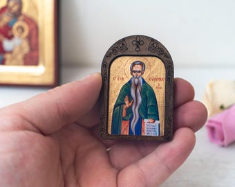 May include: A small wooden framed icon with a gold background and a painted image of a bearded man in a green robe holding a scroll. The text on the scroll reads "Ο Θεος ειναι αγιασμος" and the text below the image reads "Ο  Αγιος  Γρηγοριος  ο  Θαυματουργος".