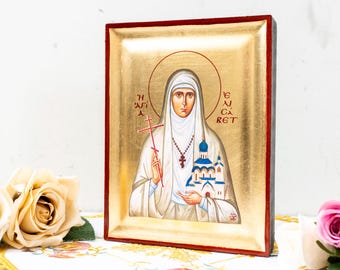 May include: An icon featuring a religious figure in white robes, holding a cross and a church. The icon has a gold background and a red frame. The image is surrounded by roses.