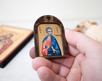 May include: A small wooden framed icon with a painted image of a man with a beard and a blue robe. The icon has Greek text on it.