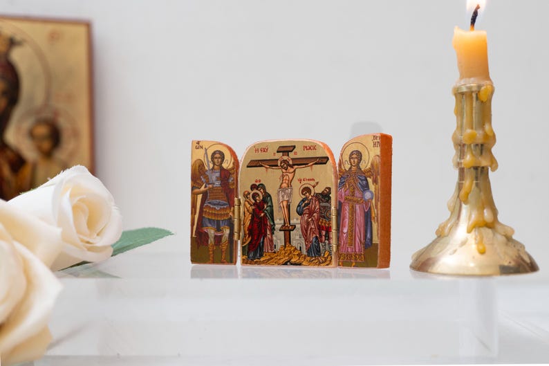 Może przedstawiać: Złoty tryptyk religijny przedstawiający sceny biblijne, w tym ukrzyżowanie, z postaciami w kolorowych szatach. Po prawej stronie zapalona świeca w złotym świeczniku. Białe r&oacute;że i ikona w tle.