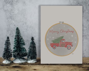 Biglietto di Natale da scaricare con cerchio da ricamo disegnato con camioncino che porta l'albero di Natale e la scritta Merry Christmas