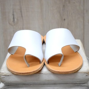 May include: White leather sandals with a thong strap and a brown leather sole.